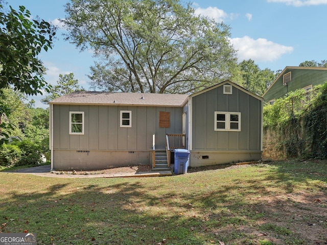 back of house with board and batten siding, an outdoor structure, a yard, a shingled roof, and crawl space