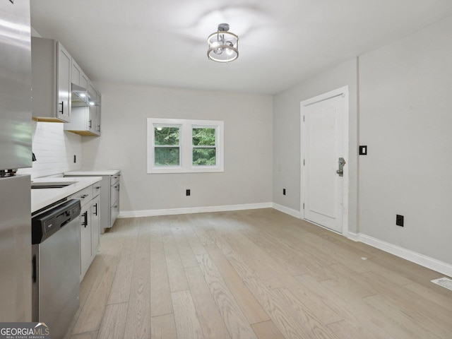 kitchen featuring light wood-type flooring, stainless steel dishwasher, baseboards, and light countertops