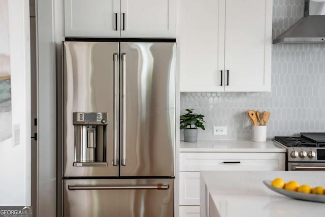 kitchen with white cabinets, wall chimney range hood, appliances with stainless steel finishes, and tasteful backsplash