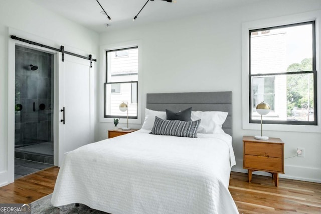 bedroom featuring light hardwood / wood-style floors, multiple windows, connected bathroom, and a barn door