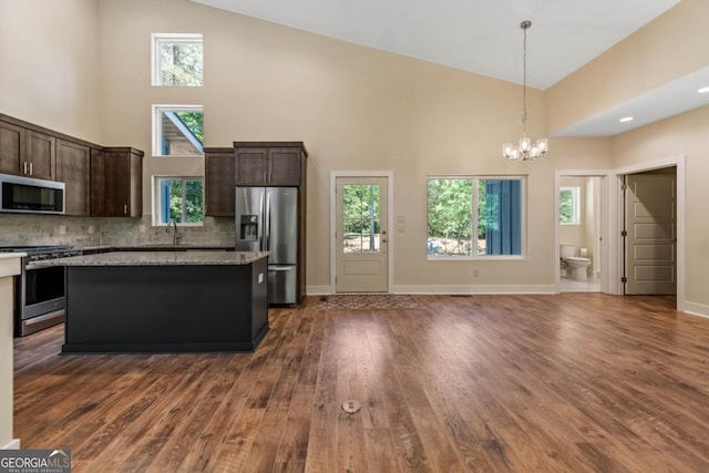 kitchen with pendant lighting, stainless steel appliances, dark wood-type flooring, dark brown cabinets, and high vaulted ceiling