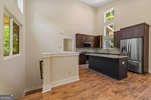 kitchen with backsplash, appliances with stainless steel finishes, dark brown cabinetry, wood finished floors, and baseboards