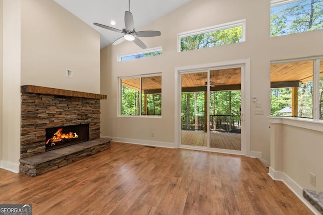 unfurnished living room with high vaulted ceiling, a healthy amount of sunlight, a stone fireplace, and wood finished floors