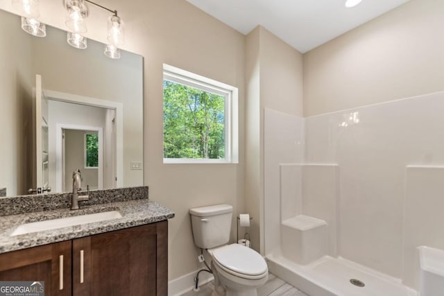 full bathroom with baseboards, vanity, toilet, and a walk in shower