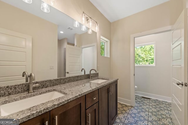 bathroom featuring toilet, a sink, baseboards, and double vanity