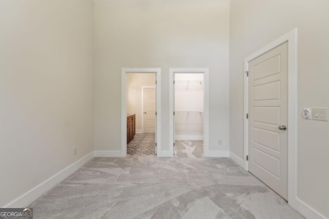 unfurnished bedroom with baseboards, light colored carpet, ensuite bath, a walk in closet, and a closet