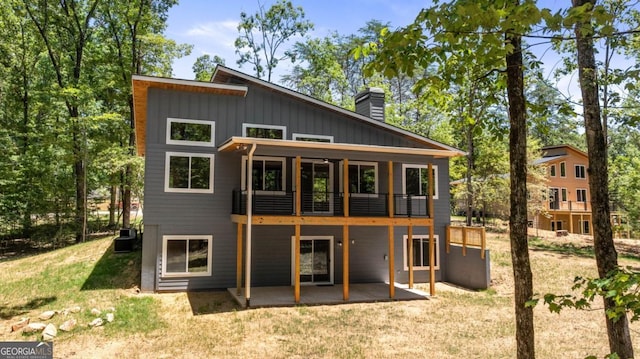 back of property with central AC unit, a lawn, a patio, a chimney, and board and batten siding