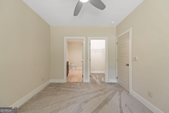 unfurnished bedroom with ensuite bathroom, carpet flooring, a walk in closet, and baseboards