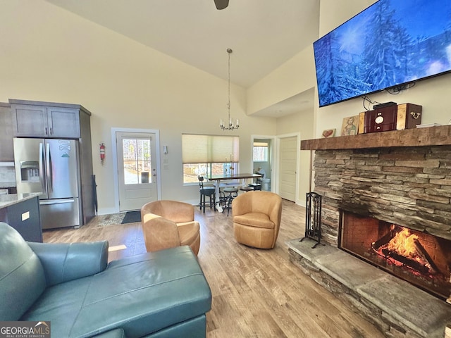 living room with baseboards, an inviting chandelier, a stone fireplace, light wood-style floors, and high vaulted ceiling