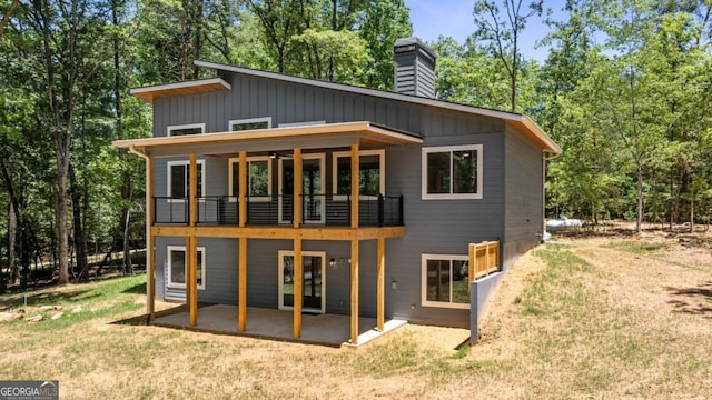 rear view of property featuring a yard, a chimney, board and batten siding, a patio area, and a balcony