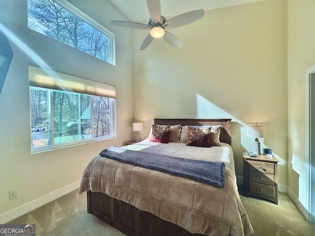 carpeted bedroom with ceiling fan, a high ceiling, multiple windows, and baseboards