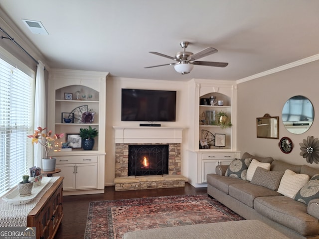 living room with ceiling fan, dark hardwood / wood-style flooring, crown molding, and a stone fireplace