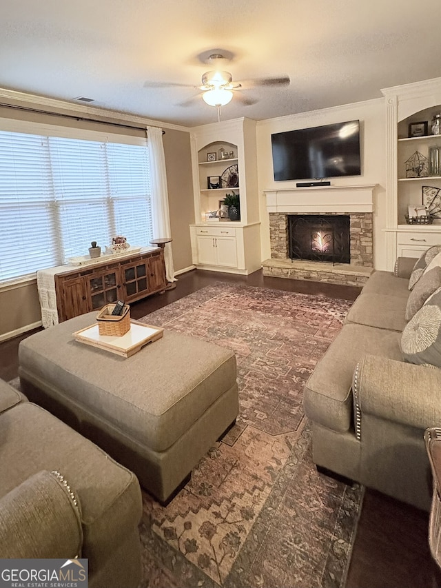 living room featuring ceiling fan, built in features, a wealth of natural light, and a stone fireplace