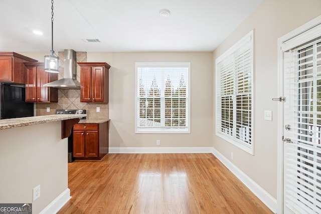 kitchen featuring pendant lighting, tasteful backsplash, stove, wall chimney exhaust hood, and black fridge