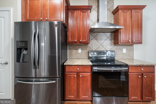 kitchen featuring black electric range, wall chimney exhaust hood, stainless steel fridge, and light stone countertops