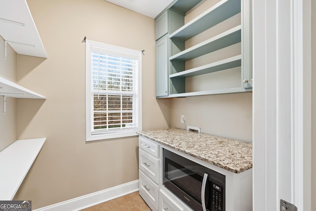 kitchen featuring light tile patterned flooring, baseboards, light stone countertops, open shelves, and stainless steel microwave