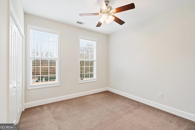 carpeted spare room with ceiling fan, visible vents, and baseboards