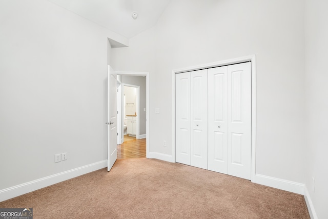 unfurnished bedroom featuring high vaulted ceiling, a closet, carpet flooring, and baseboards