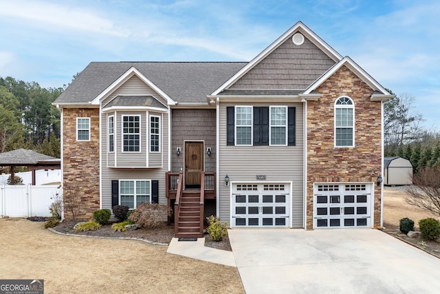 split foyer home with roof with shingles, fence, a garage, stone siding, and driveway