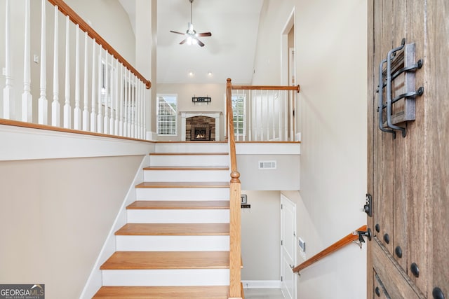 stairs with visible vents, a high ceiling, a ceiling fan, wood finished floors, and baseboards