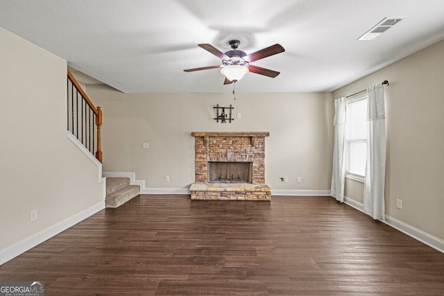 unfurnished living room with ceiling fan, a stone fireplace, and dark hardwood / wood-style flooring