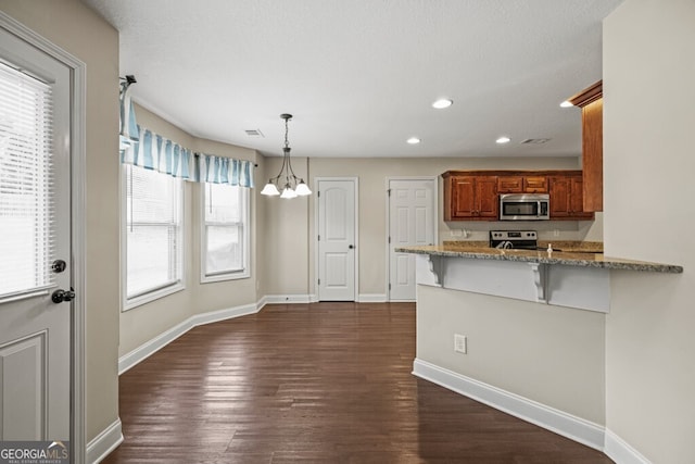 kitchen featuring a kitchen bar, light stone countertops, appliances with stainless steel finishes, decorative light fixtures, and kitchen peninsula