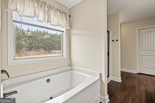 bathroom with hardwood / wood-style flooring, a textured ceiling, and a bath