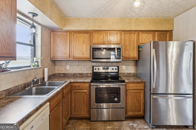 kitchen with appliances with stainless steel finishes, a textured ceiling, hanging light fixtures, sink, and backsplash