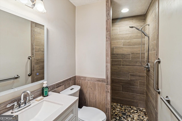 bathroom with tiled shower, toilet, tile walls, and vanity