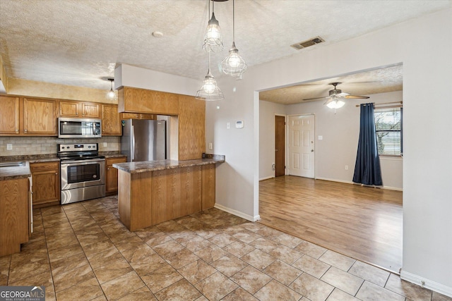 kitchen with a textured ceiling, pendant lighting, appliances with stainless steel finishes, tasteful backsplash, and kitchen peninsula