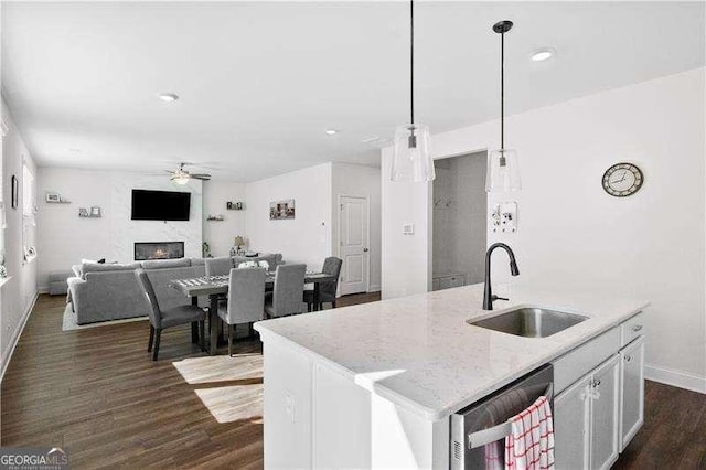 kitchen featuring decorative light fixtures, dark wood finished floors, a center island with sink, a sink, and a lit fireplace