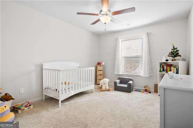 carpeted bedroom with a ceiling fan, a crib, and baseboards