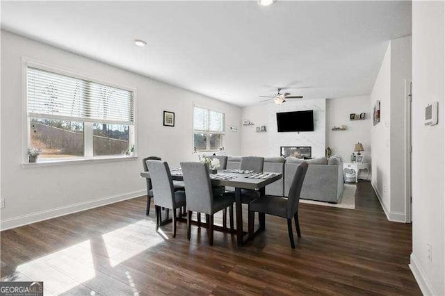 dining space with ceiling fan, a fireplace, baseboards, and dark wood finished floors