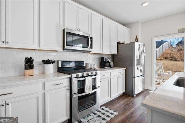 kitchen featuring appliances with stainless steel finishes, white cabinets, decorative backsplash, and light stone countertops