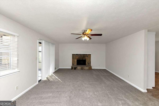 unfurnished living room featuring carpet floors, ceiling fan, a textured ceiling, and a stone fireplace