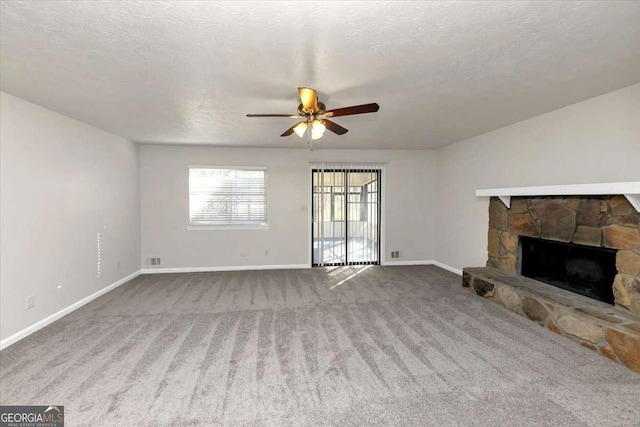 unfurnished living room featuring ceiling fan, a stone fireplace, a textured ceiling, and carpet floors