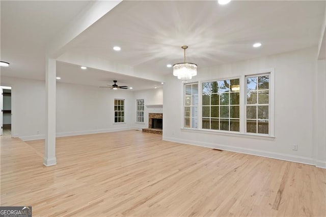 unfurnished living room featuring light wood-type flooring, ceiling fan with notable chandelier, and a fireplace