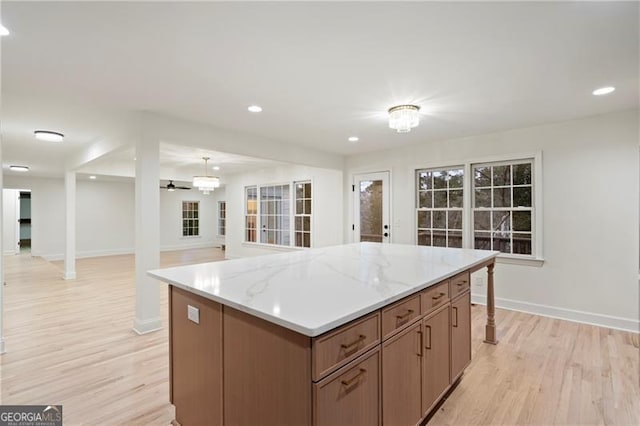 kitchen featuring light stone countertops, a center island, hanging light fixtures, and light hardwood / wood-style floors