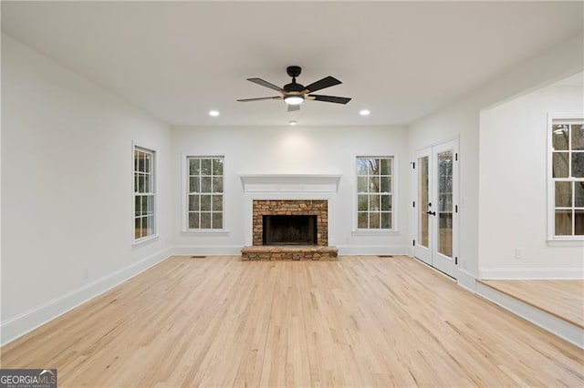 unfurnished living room featuring a fireplace, plenty of natural light, light hardwood / wood-style flooring, and ceiling fan