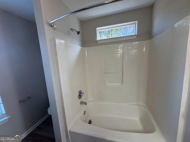 bathroom featuring a textured ceiling, bathing tub / shower combination, and toilet