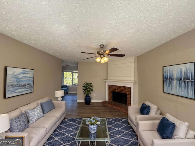 living room with ceiling fan, dark wood-type flooring, a textured ceiling, and a brick fireplace