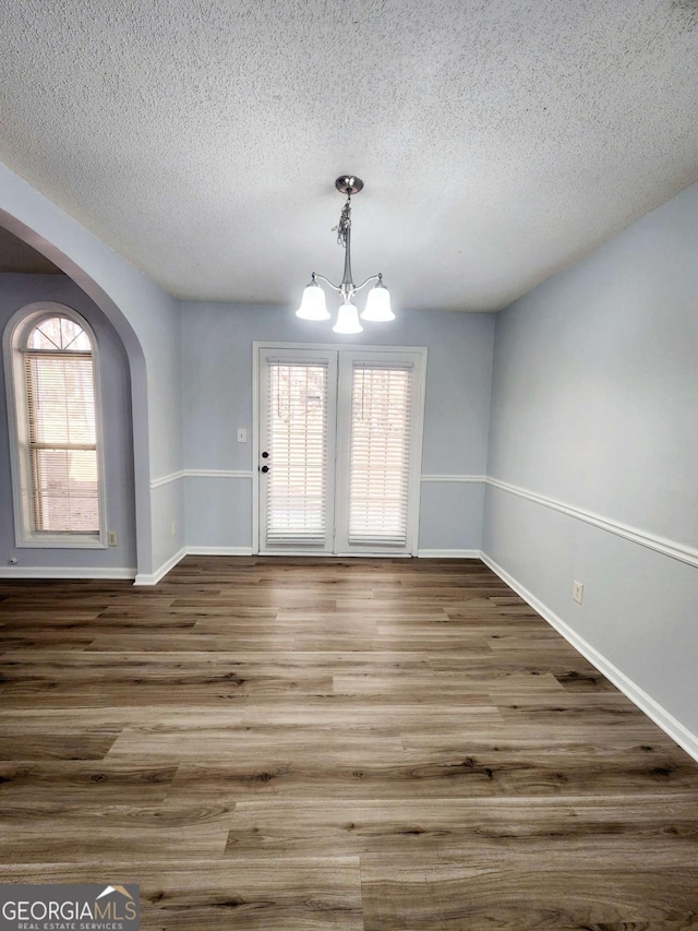 unfurnished dining area with a chandelier, a textured ceiling, and wood-type flooring