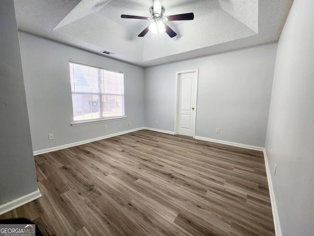 unfurnished room with hardwood / wood-style flooring, ceiling fan, a textured ceiling, and a tray ceiling