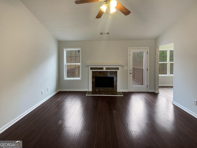 unfurnished living room featuring a stone fireplace, dark hardwood / wood-style floors, lofted ceiling, and ceiling fan