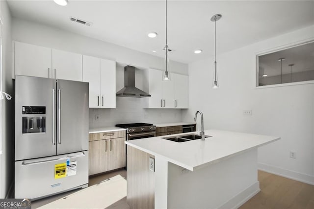 kitchen with wall chimney exhaust hood, sink, hanging light fixtures, appliances with stainless steel finishes, and a kitchen island with sink