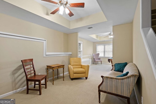 living area featuring ceiling fan, light colored carpet, and a raised ceiling