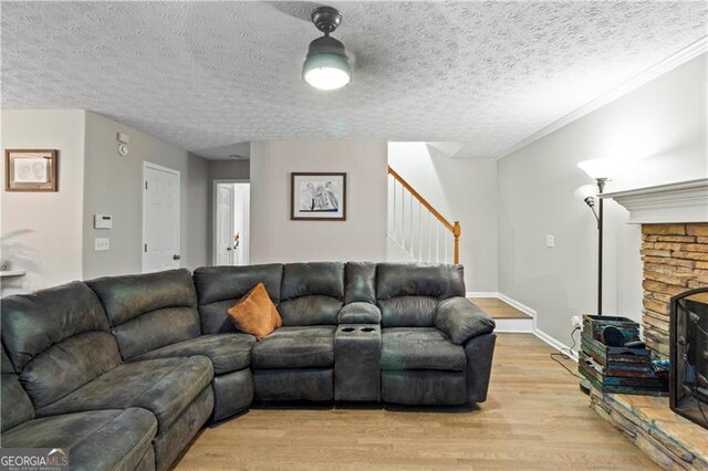 living room featuring a stone fireplace, a textured ceiling, and light wood-type flooring