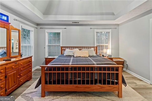 bedroom with a tray ceiling and light hardwood / wood-style flooring