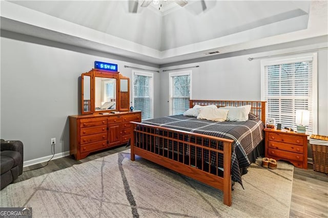 bedroom with ceiling fan, lofted ceiling, a raised ceiling, and hardwood / wood-style floors