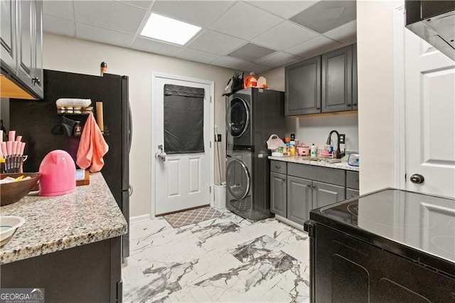 kitchen with sink, a paneled ceiling, electric range, light stone counters, and stacked washer / drying machine